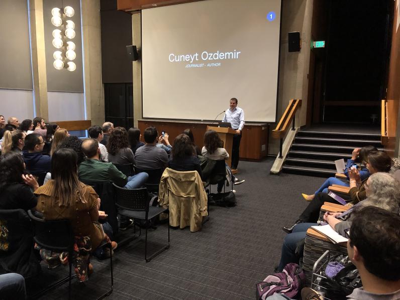 Cüneyt Ozdemir standing before a large crowd introducing his presentation.