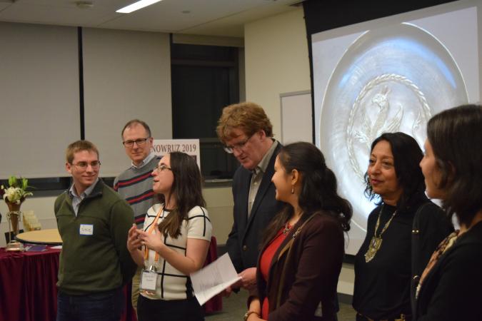 A line of Ancient Iran Day organizers stand in front of a presentation discussing the days events